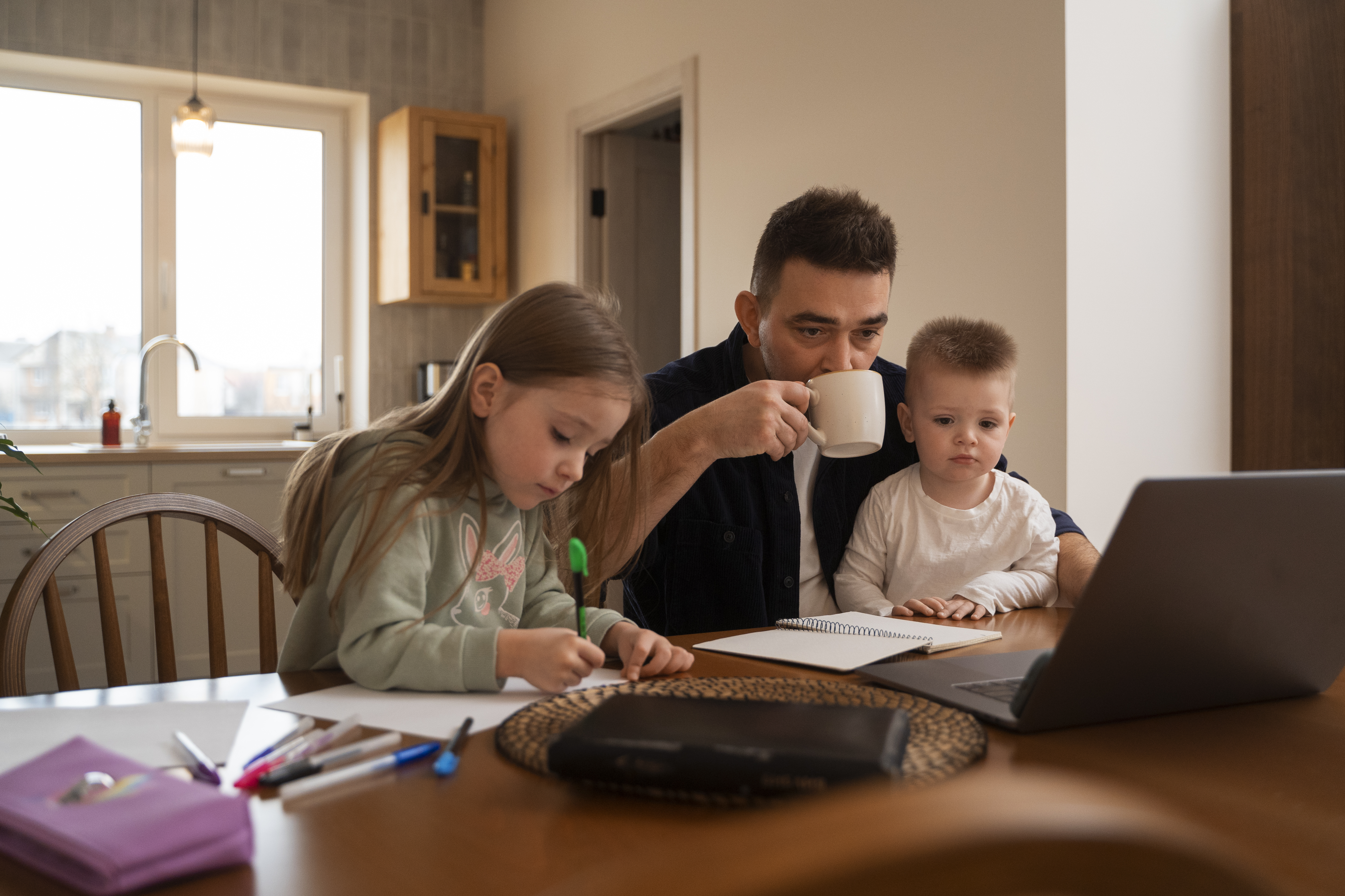 Father working on a laptop at home with two kids